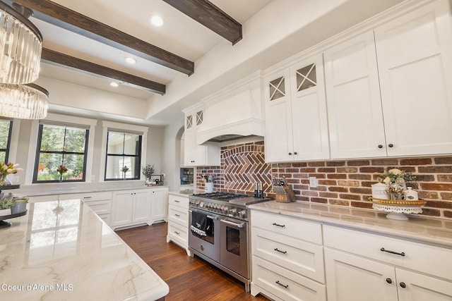 kitchen featuring tasteful backsplash, light stone counters, premium range hood, white cabinets, and double oven range