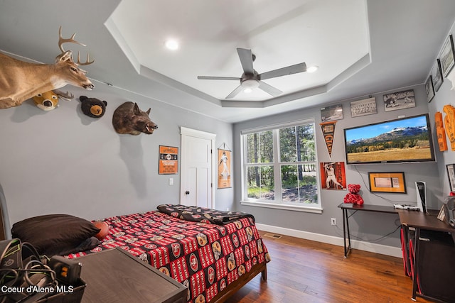 bedroom featuring a tray ceiling, a ceiling fan, visible vents, hardwood / wood-style floors, and baseboards