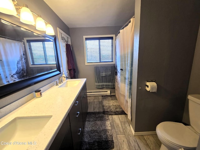 bathroom featuring a sink, double vanity, toilet, baseboard heating, and wood finished floors