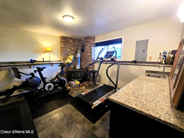 workout room featuring a wood stove, a textured ceiling, electric panel, and a sink