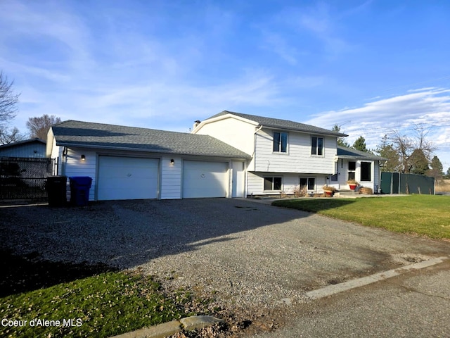 split level home featuring gravel driveway, fence, an attached garage, roof with shingles, and a front yard