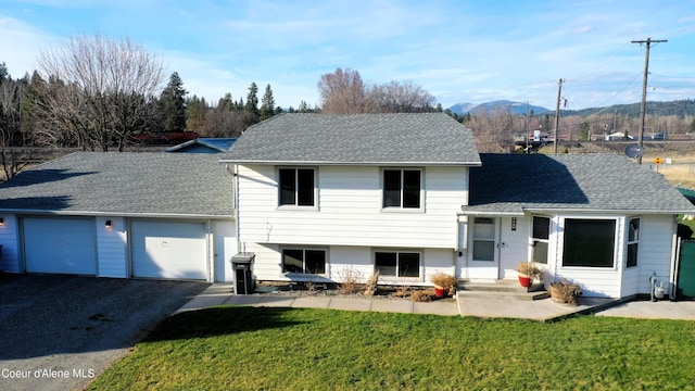 rear view of house featuring a yard, an attached garage, driveway, roof with shingles, and a mountain view