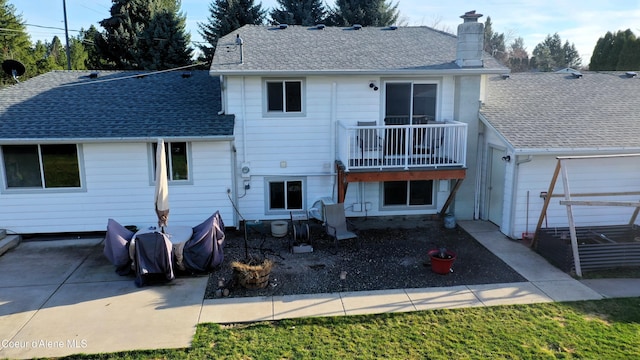 rear view of house featuring a chimney, a balcony, a patio, and a shingled roof