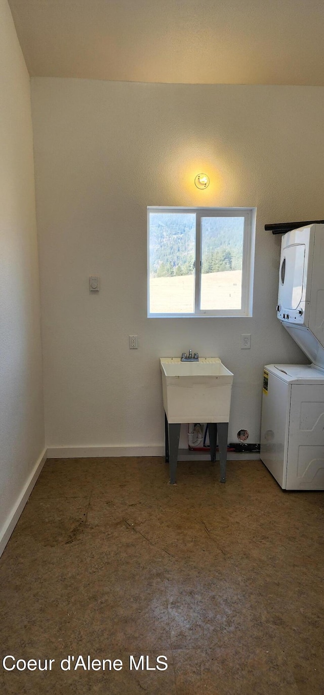 laundry room featuring a sink, laundry area, stacked washer / drying machine, and baseboards