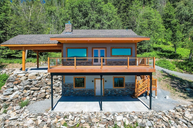 back of property featuring a chimney, stone siding, a patio area, and a deck