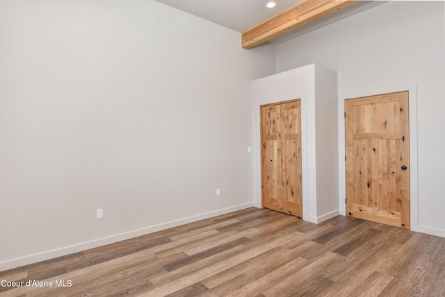 unfurnished room featuring baseboards, a towering ceiling, light wood-style floors, and beamed ceiling