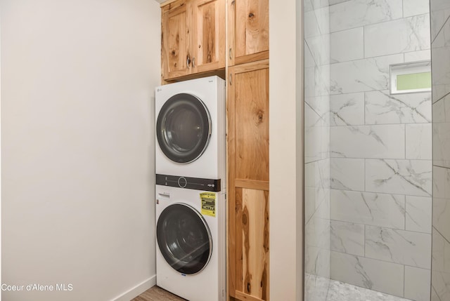 clothes washing area with baseboards and stacked washing maching and dryer