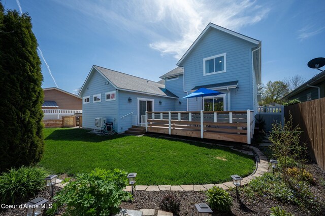 rear view of house with fence, a wooden deck, a lawn, and roof with shingles