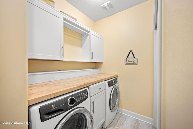 laundry area with visible vents, washing machine and clothes dryer, cabinet space, baseboards, and light wood-style flooring