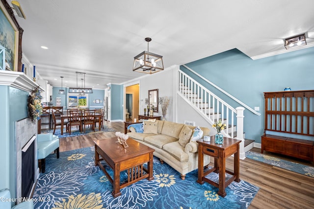 living room featuring a notable chandelier, baseboards, wood finished floors, ornamental molding, and stairway