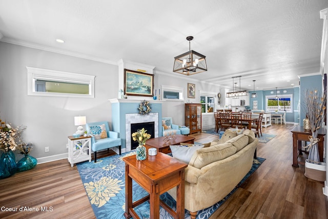 living area with crown molding, a chandelier, baseboards, wood finished floors, and a tile fireplace