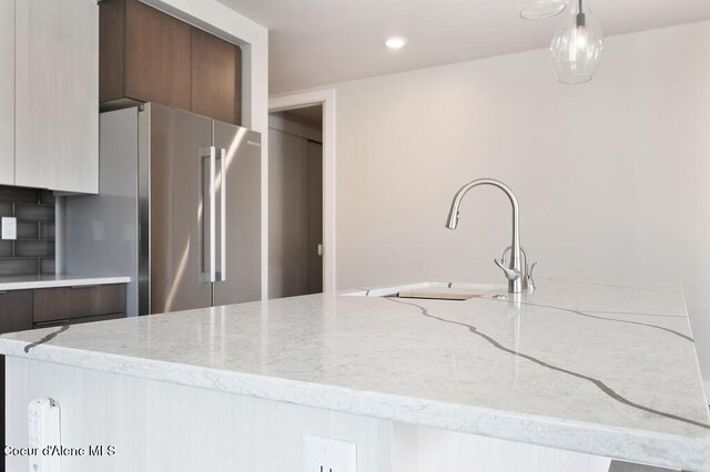 1579 W Riverstone Dr # 306, Coeur Dalene, ID 83814 - kitchen with light stone counters, a sink, modern cabinets, freestanding refrigerator, and pendant lighting