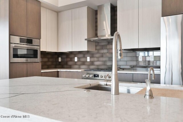 1579 W Riverstone Dr # 306, Coeur Dalene, ID 83814 - kitchen with wall chimney exhaust hood, stainless steel appliances, backsplash, modern cabinets, and light stone counters