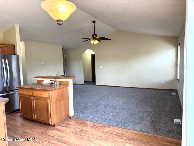 2359 N Alfalfa Loop, Post Falls, ID 83854 - kitchen with vaulted ceiling, a ceiling fan, arched walkways, freestanding refrigerator, and brown cabinetry
