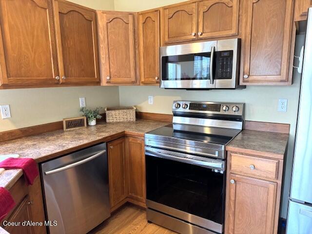 2359 N Alfalfa Loop, Post Falls, ID 83854 - kitchen featuring brown cabinets, dark countertops, light wood-style flooring, and appliances with stainless steel finishes