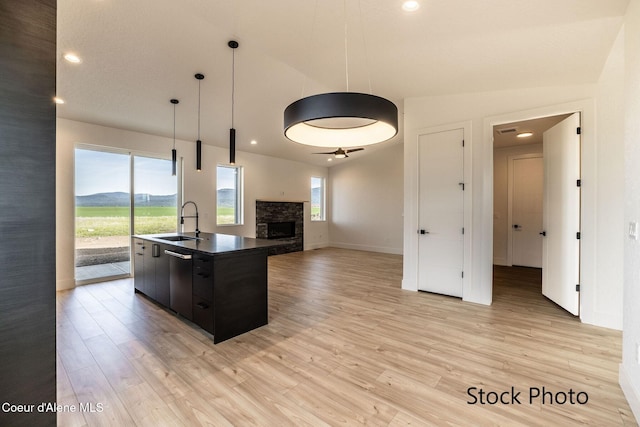 11506 N Clapton Ln, Rathdrum, ID 83858 - kitchen featuring a sink, light wood-style flooring, dark countertops, an island with sink, and a fireplace