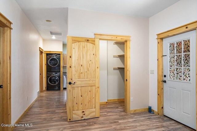 foyer with stacked washer / drying machine, baseboards, wood finished floors, and visible vents