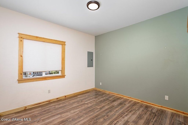 unfurnished room with wood finished floors, electric panel, and baseboards