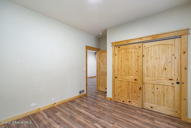 unfurnished bedroom featuring baseboards, wood finished floors, and visible vents