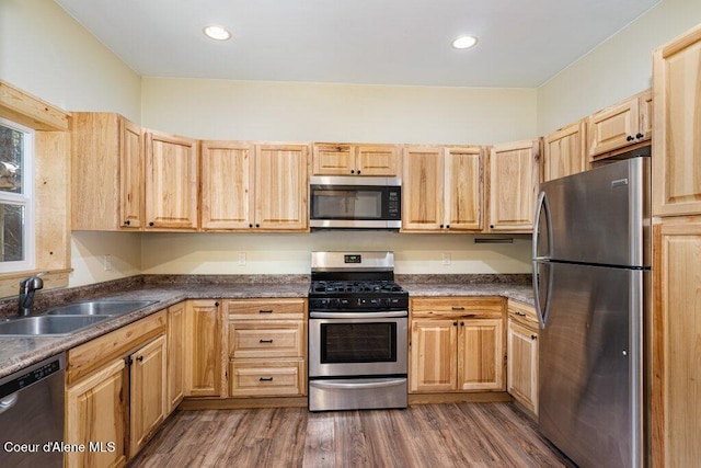 kitchen with stainless steel appliances, a sink, dark wood finished floors, dark countertops, and light brown cabinets