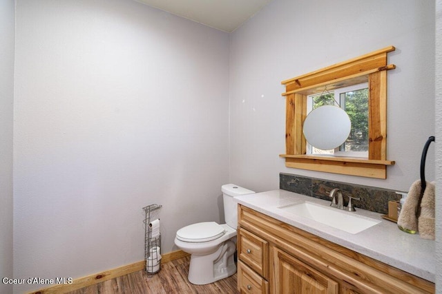 half bath featuring baseboards, wood finished floors, toilet, and vanity