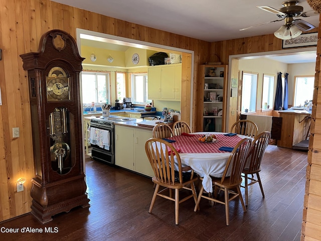 dining room featuring dark wood-style floors, a ceiling fan, and wooden walls