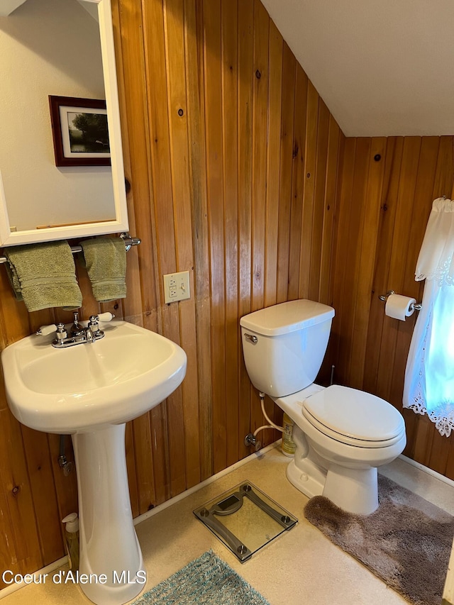 bathroom with toilet, wooden walls, and baseboards