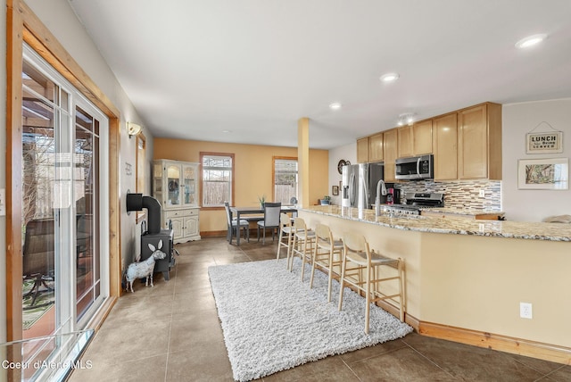 kitchen with appliances with stainless steel finishes, light brown cabinets, tasteful backsplash, light stone countertops, and recessed lighting