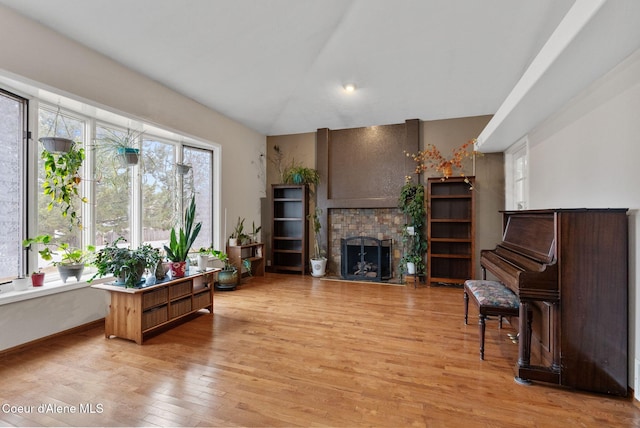living area with light wood-type flooring, baseboards, vaulted ceiling, and a brick fireplace