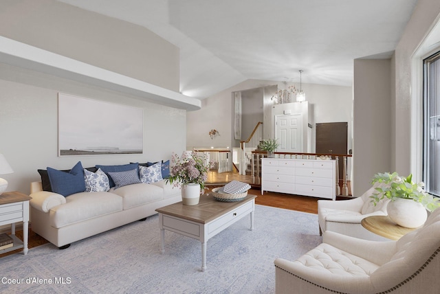 living area with vaulted ceiling, wood finished floors, and stairs