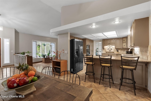 kitchen featuring a kitchen breakfast bar, a sink, black appliances, a peninsula, and tasteful backsplash