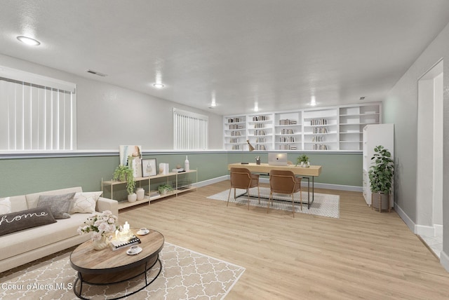 living room featuring wood finished floors, visible vents, built in shelves, and baseboards