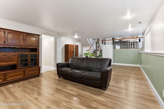 living room with stairway, baseboards, visible vents, and light wood finished floors