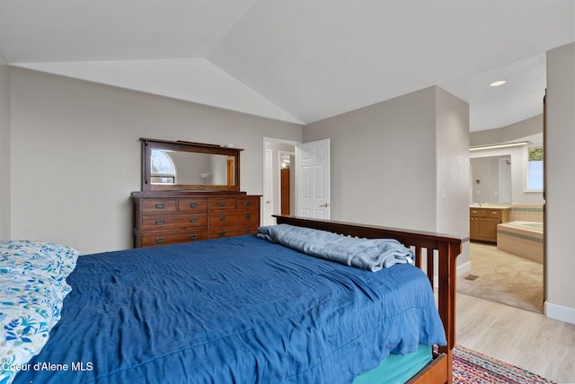 bedroom featuring lofted ceiling, light wood finished floors, baseboards, and ensuite bathroom