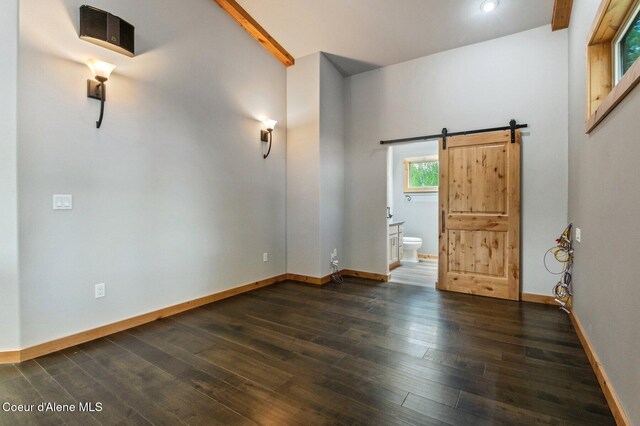 interior space featuring baseboards, lofted ceiling with beams, dark wood-style floors, and a barn door