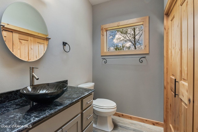 half bathroom with vanity, baseboards, toilet, and wood finished floors