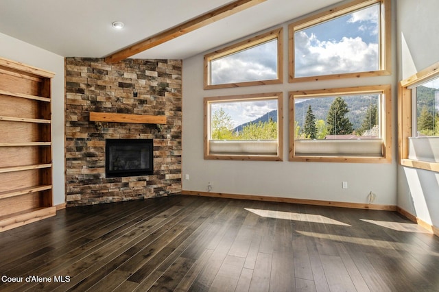 unfurnished living room with a stone fireplace, baseboards, hardwood / wood-style floors, and beamed ceiling