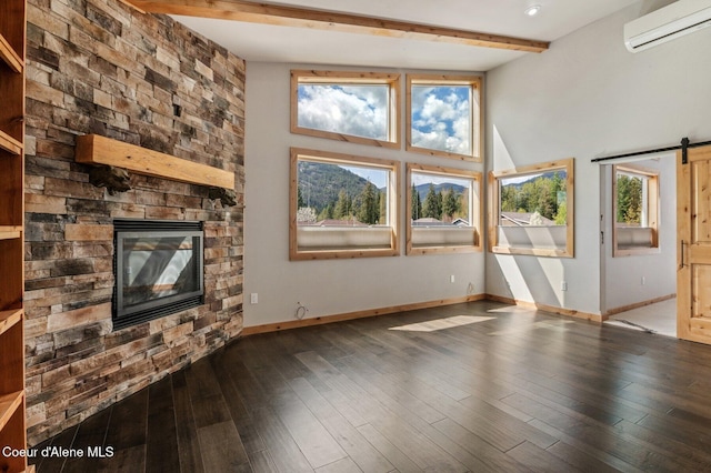 unfurnished living room featuring a fireplace, beamed ceiling, baseboards, an AC wall unit, and a barn door
