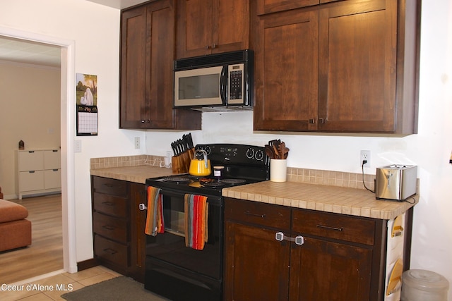 kitchen with light tile patterned floors, black range with electric cooktop, dark brown cabinetry, crown molding, and light countertops