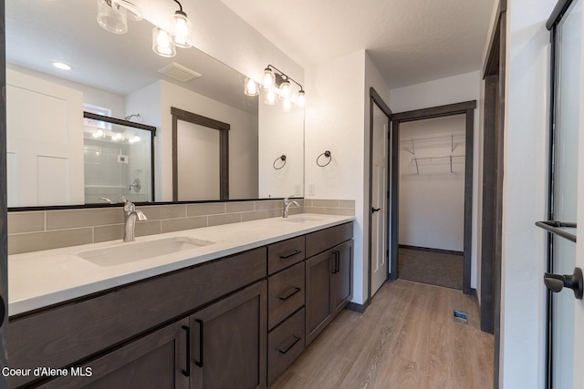 bathroom featuring backsplash, wood finished floors, a stall shower, and a sink
