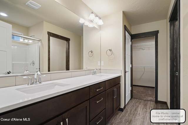 bathroom featuring a shower with shower door, wood finished floors, visible vents, and a sink