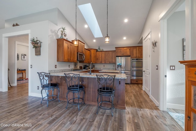 5867 W Sparrowhawk Dr, Rathdrum, ID 83858 - kitchen with light stone counters, vaulted ceiling with skylight, brown cabinets, a peninsula, and appliances with stainless steel finishes