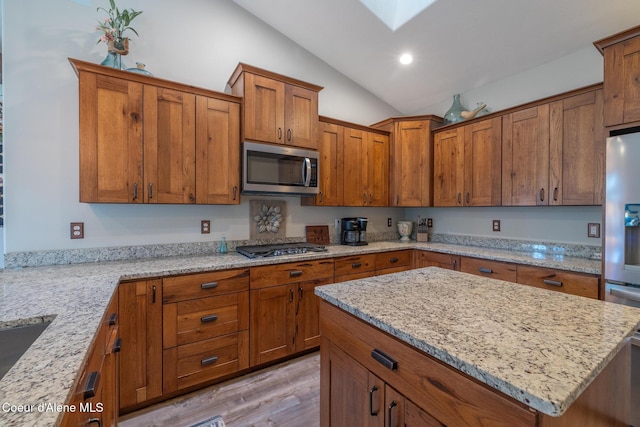 5867 W Sparrowhawk Dr, Rathdrum, ID 83858 - kitchen with stainless steel appliances, light wood-style floors, brown cabinets, and vaulted ceiling with skylight