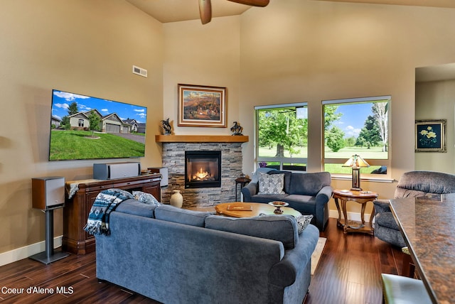 living area featuring a ceiling fan, a stone fireplace, baseboards, dark wood-style flooring, and visible vents
