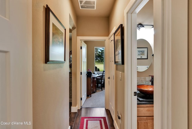 hall featuring dark wood-type flooring, visible vents, and a sink