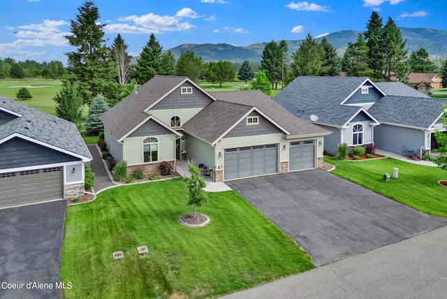 view of front facade featuring a front lawn, a mountain view, driveway, stone siding, and a garage