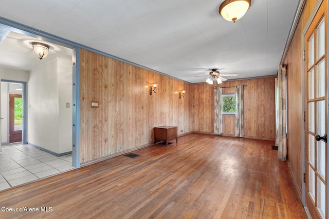 empty room with wood-type flooring, wooden walls, baseboards, and ceiling fan