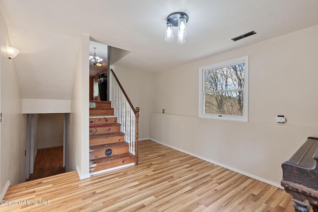 stairway featuring wood finished floors, visible vents, baseboards, and a notable chandelier