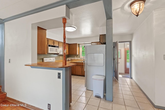 kitchen with a peninsula, white microwave, stove, brown cabinets, and refrigerator