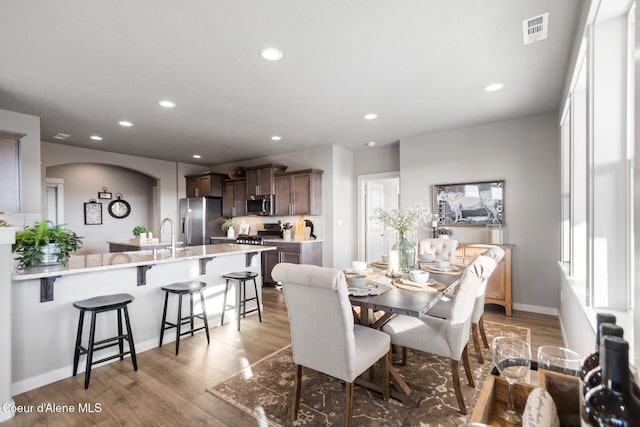 dining room featuring arched walkways, baseboards, visible vents, recessed lighting, and light wood-style floors